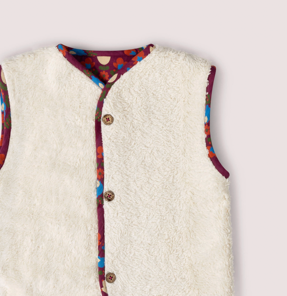 Little Green Rascals Folk Birds reversible gilet — close-up of the upper sherpa side showing the fluffy natural cream organic sherpa with folk birds print contrast binding trim at the neckline and armhole, and branded coconut shell buttons