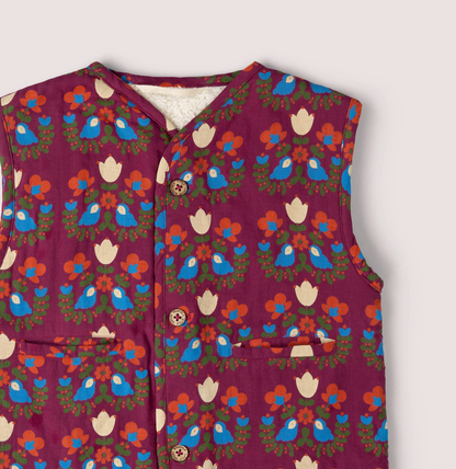 Little Green Rascals Folk Birds reversible gilet — close-up of the upper print side showing the bold folk art print detail of blue birds, cream tulips and orange flowers on burgundy, with the natural cream sherpa lining visible at the open neckline and the branded coconut shell buttons
