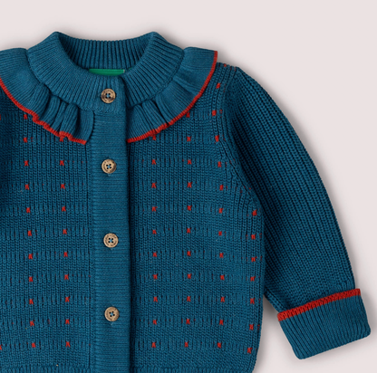 Little Green Rascals Midnight Frill Snuggly Cardigan — close-up of the upper body and collar showing the knitted ruffle frill collar with red contrast edge trim, the scattered red dash stitch pattern woven into the midnight teal chunky knit, branded coconut shell buttons, and ribbed cuff with red contrast stripe