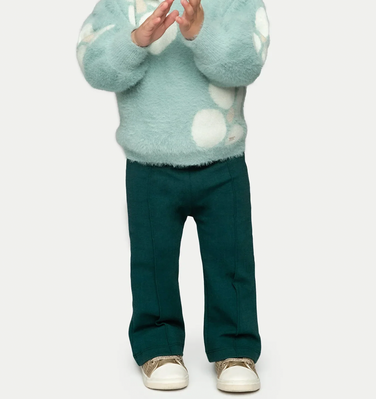 Mayoral girls' emerald green flared trousers styled on a child with a pale blue fluffy polka dot jumper and gold trainers on a white background