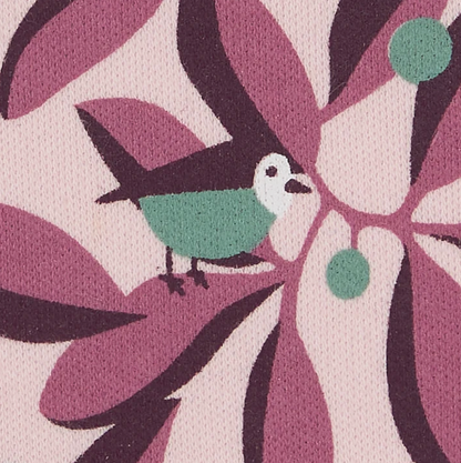 Close-up — individual bird in sharp focus (plum wing, teal body, white cheek, dark beak); teal berry cluster; leaf layers; jersey fabric texture.