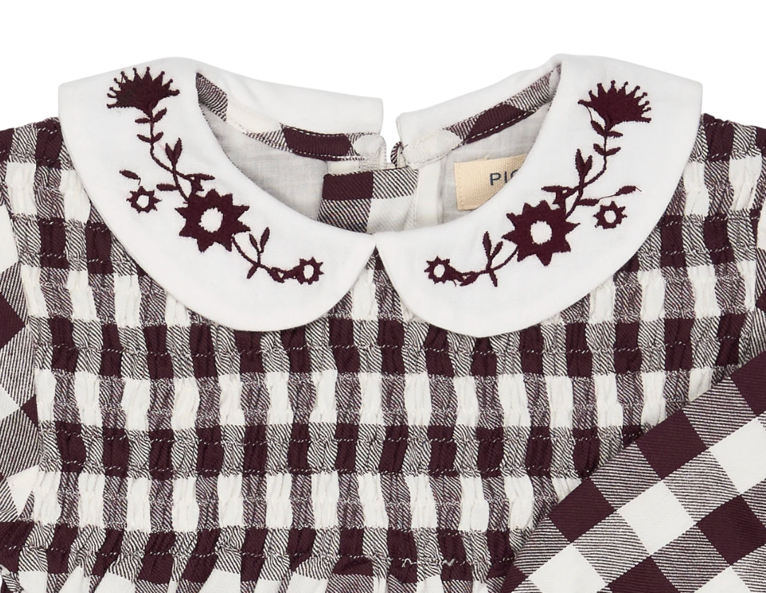 Close-up — collar embroidery in sharp focus; individual flower heads, star buds and stems; Pigeon Organics label; smocking construction; woven fabric texture.