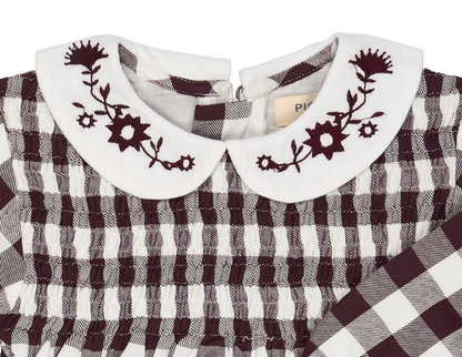 Close-up — collar embroidery in sharp focus; individual flower heads, star buds and stems; Pigeon Organics label; smocking construction; woven fabric texture.