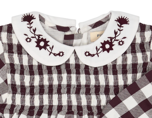 Close-up — collar embroidery in sharp focus; individual flower heads, star buds and stems; Pigeon Organics label; smocking construction; woven fabric texture.