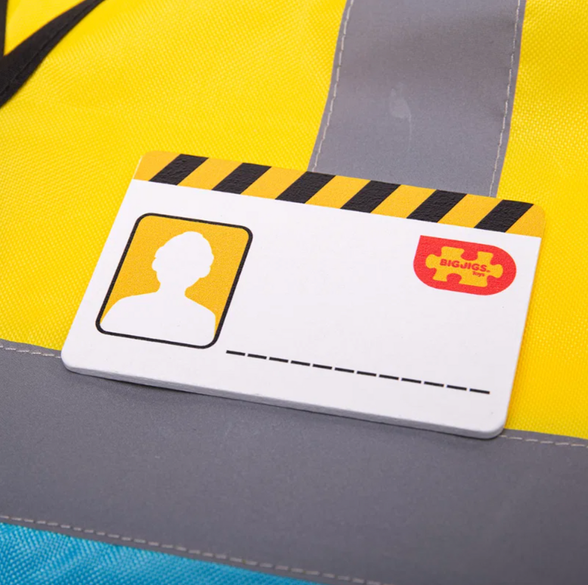 Close-up — ID badge detail; hazard stripe header; silhouette photo box; Bigjigs logo 