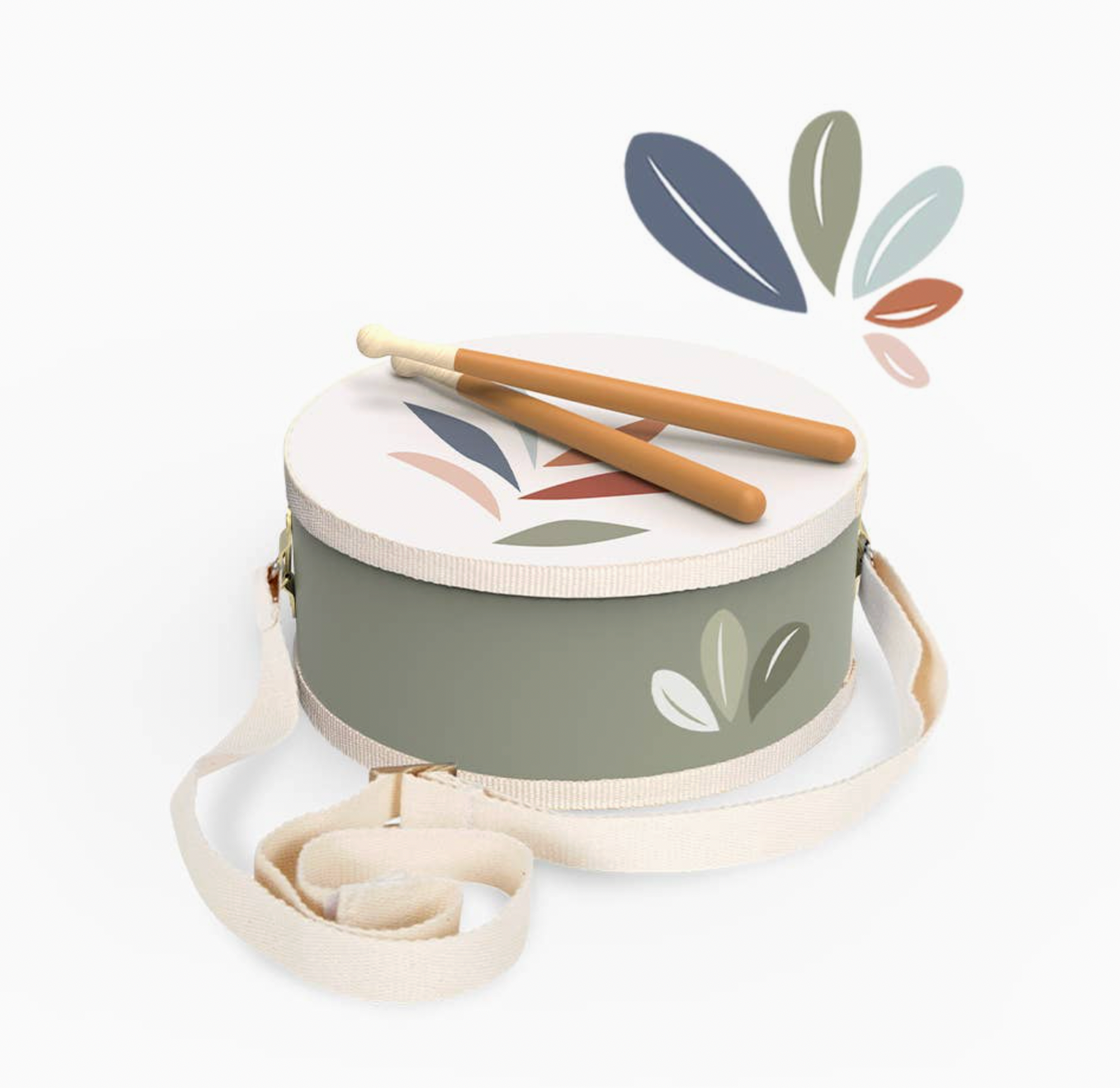 Angled overhead product shot — sage green drum, white botanical leaf head, two drumsticks crossed on top, cream strap trailing; decorative leaf graphic top right