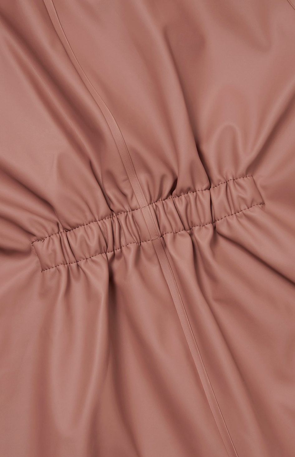  Extreme close-up of the elasticated back waist gathering on the Grass & Air Rose puddle suit; ruched and gathered rose waterproof fabric radiating outward from the central horizontal elasticated waistband panel; vertical seam lines running through the gathered fabric sections on either side; fine parallel stitching detail on the elasticated band visible; shows the construction of the back shaping panel that provides a comfortable shaped fit when worn over layers