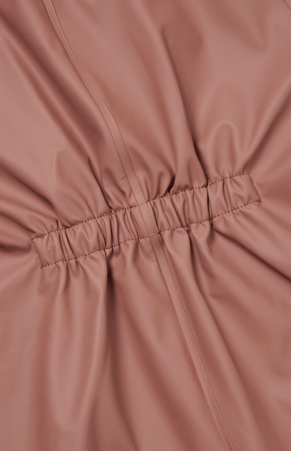  Extreme close-up of the elasticated back waist gathering on the Grass & Air Rose puddle suit; ruched and gathered rose waterproof fabric radiating outward from the central horizontal elasticated waistband panel; vertical seam lines running through the gathered fabric sections on either side; fine parallel stitching detail on the elasticated band visible; shows the construction of the back shaping panel that provides a comfortable shaped fit when worn over layers