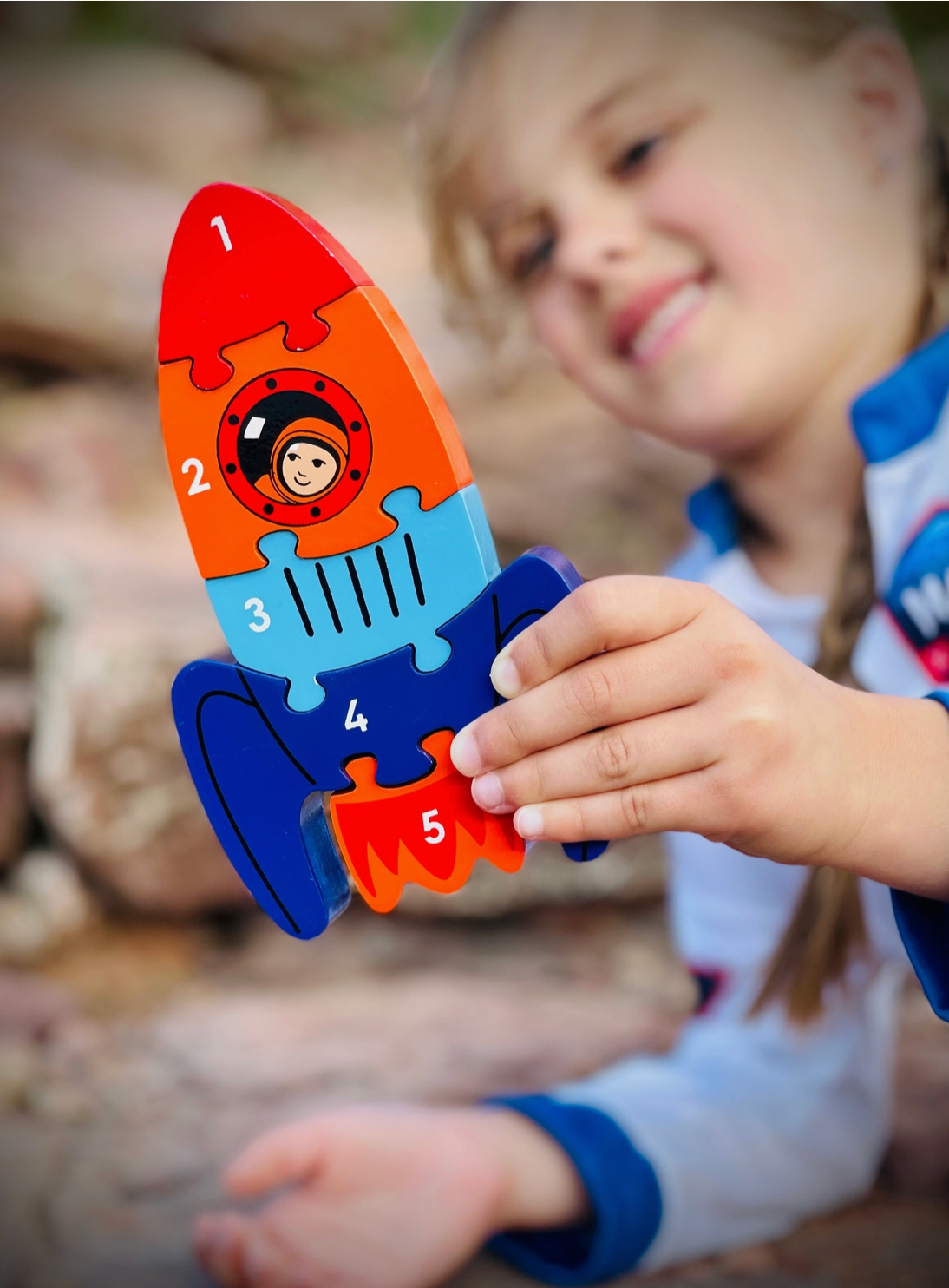 Lifestyle — young girl holding rocket upright in both hands, big grin, outdoor bokeh background; scale and play pattern clearly visible