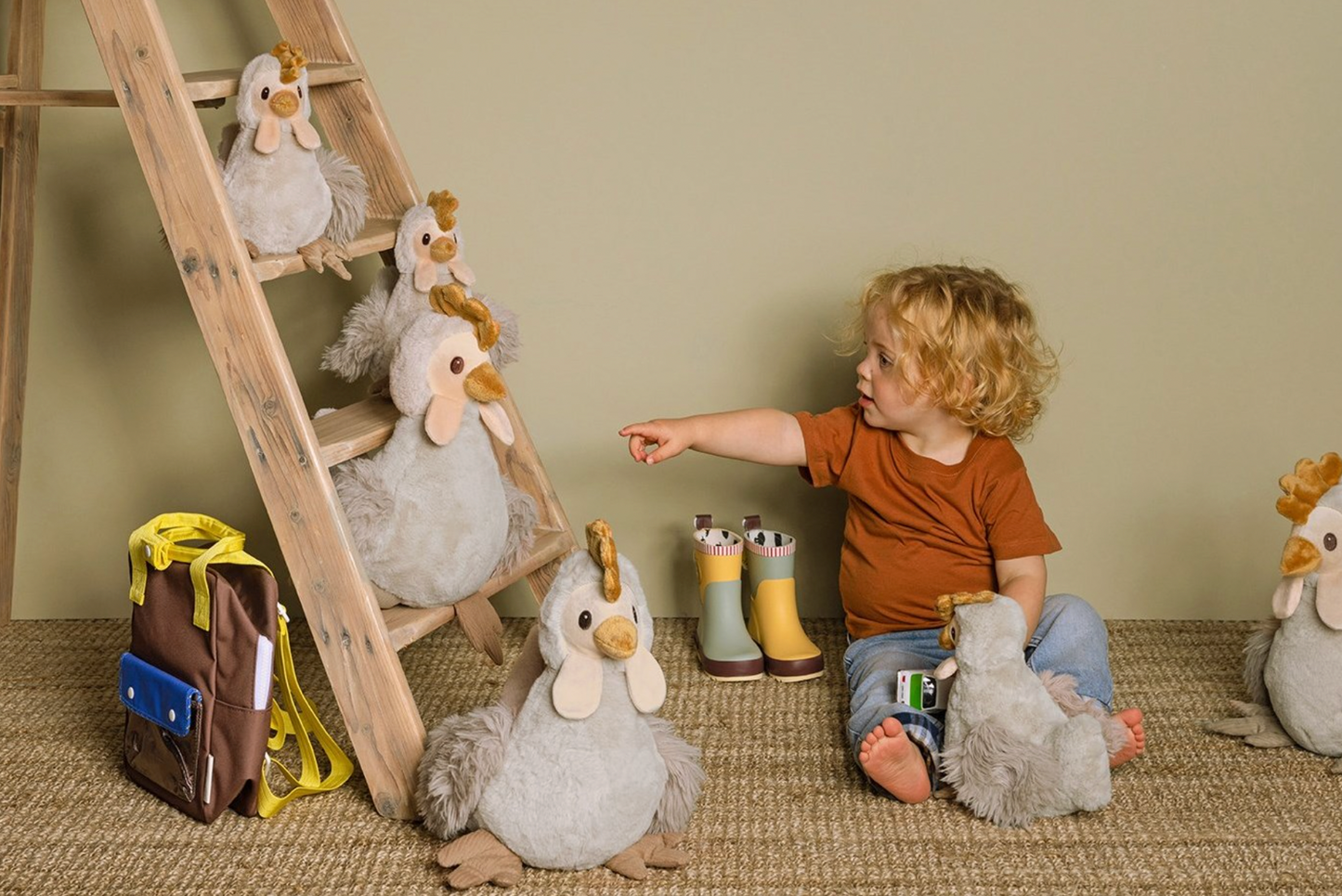 Lifestyle — curly-haired toddler pointing at 5 Carise chickens on a ladder; multiple sizes; sage green wall; jute rug; wellington boots