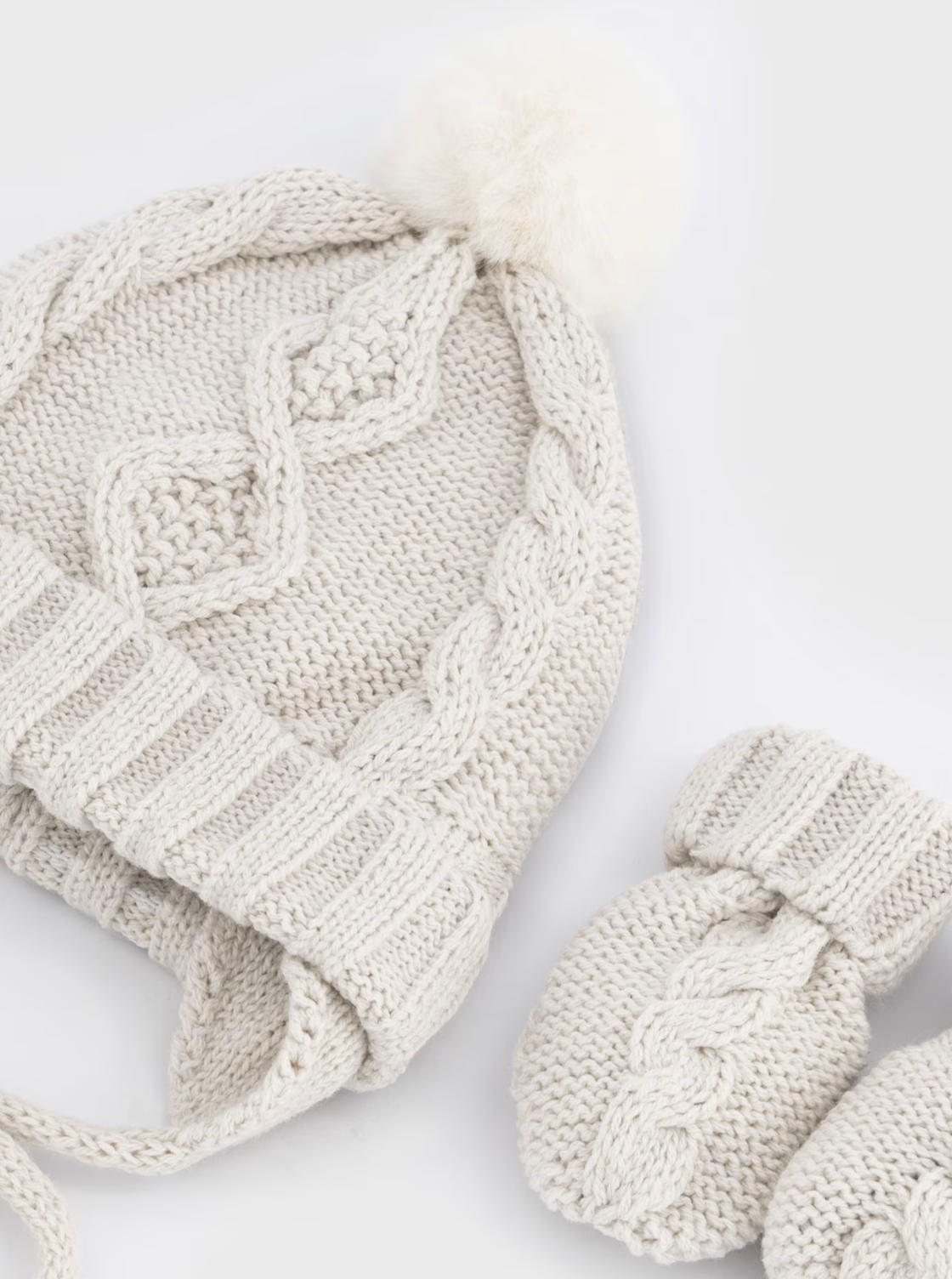 lat lay close-up on white — hat showing full cable knit detail; mittens beside; overhead angle