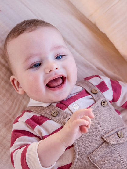 Lifestyle — laughing blue-eyed baby on cream surface; full set worn; hero candidate