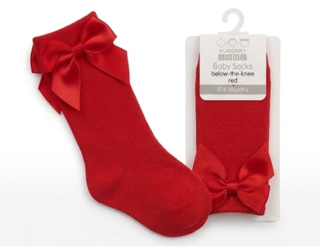 Nursery Time Baby Knee High Socks with Bow in Red shown on a white background alongside original retail packaging; bold cherry red soft fine-knit cotton socks with a long length sitting below the knee; each sock has a large satin ribbon bow in matching cherry red at the back of the calf with two loops and two tails; retail packaging on the right is a white card hanger pack labelled Baby Socks, below-the-knee, red, 0 to 6 Months with the Burbery Baby brand mark
