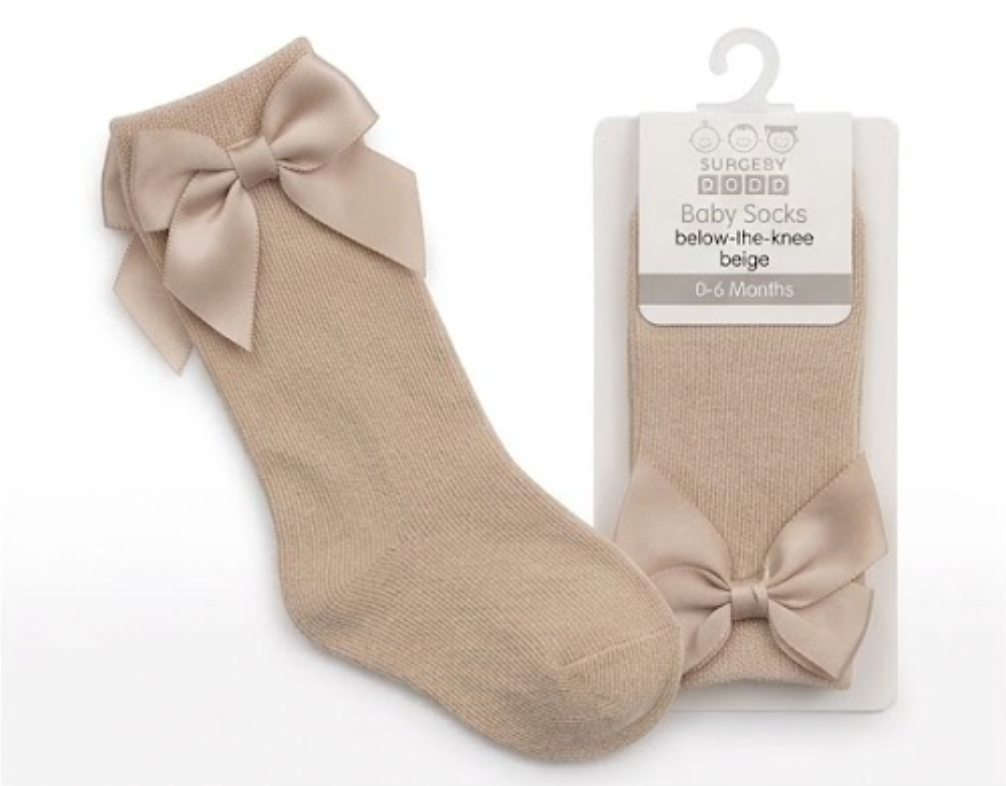 Nursery Time Baby Knee High Socks with Bow in Taupe shown on a white background alongside original retail packaging; warm sandy beige or linen-taupe soft fine-knit cotton socks with a long length sitting below the knee; each sock has a large full satin ribbon bow in matching taupe-beige at the back of the calf with two loops and two tails; retail packaging on the right is a white card hanger pack labelled Baby Socks, below-the-knee, beige, 0 to 6 Months with the Burbery Baby brand mark