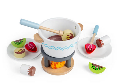 Bigjigs Toys Chocolate Pot for Two on a white background with both dipping sticks inserted into the fondue pot, one holding a pale yellow bear-face biscuit; two white plates flank the pot each holding red strawberry, kiwi and biscuit treat pieces with painted chocolate drizzle; lone kiwi slice rests to the lower right