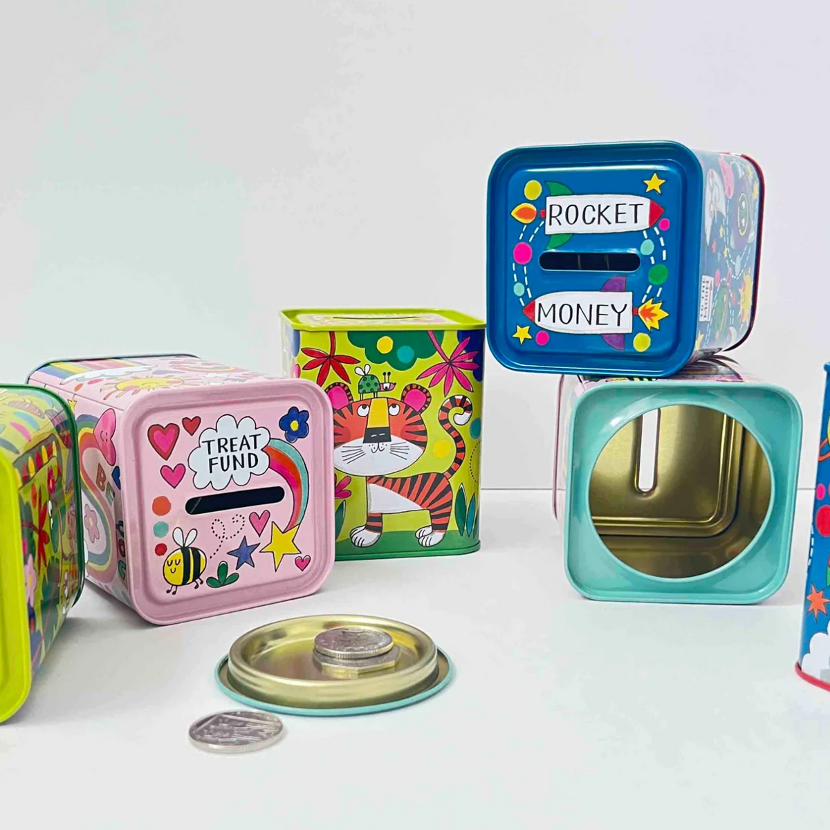 Rachel Ellen illustrated children's money boxes displayed together, including the blue dinosaur design with a top coin slot