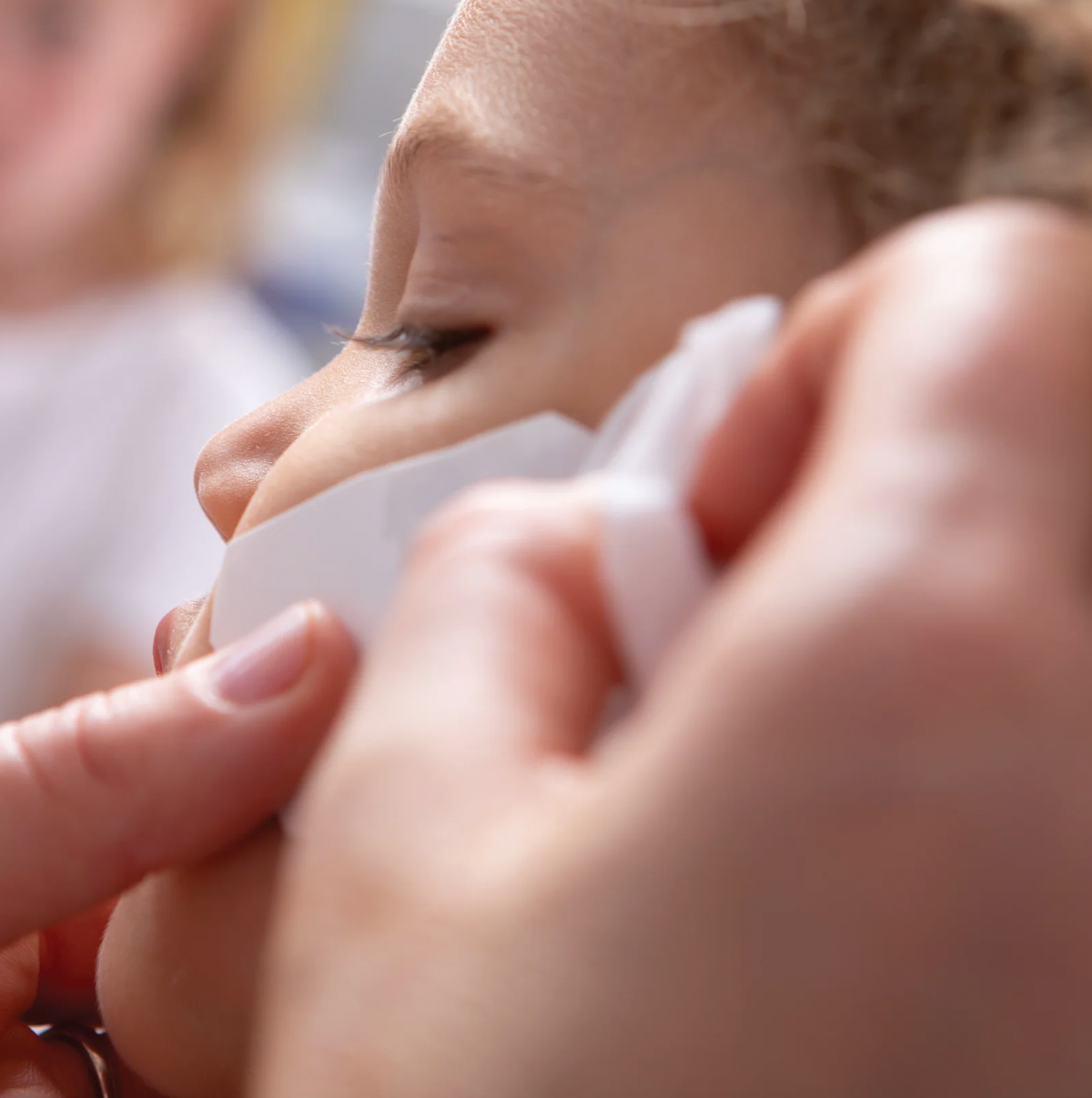 Close-up of hands peeling the backing from a temporary tattoo before applying it to skin, demonstrating the Rachel Ellen tattoo application process
