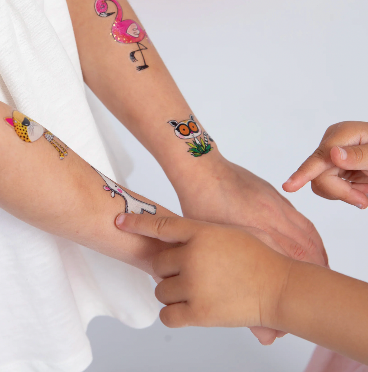 Close-up of a child pointing to Rachel Ellen Love Our Planet temporary tattoos on the forearms, including pink flamingo, leopard, owl and white animal designs