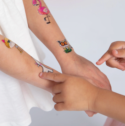 Close-up of a child pointing to Rachel Ellen Love Our Planet temporary tattoos on the forearms, including pink flamingo, leopard, owl and white animal designs