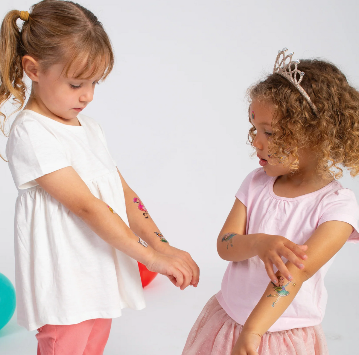 Two children showing colourful Rachel Ellen Love Our Planet temporary tattoos on their arms, including animal designs, while wearing white and pale pink clothing