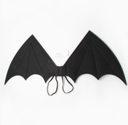 Child wearing Molly & Rose black fabric bat wings over a checked dress; pointed wing tips, scalloped lower edges, stitched panel lines and black elastic straps visible