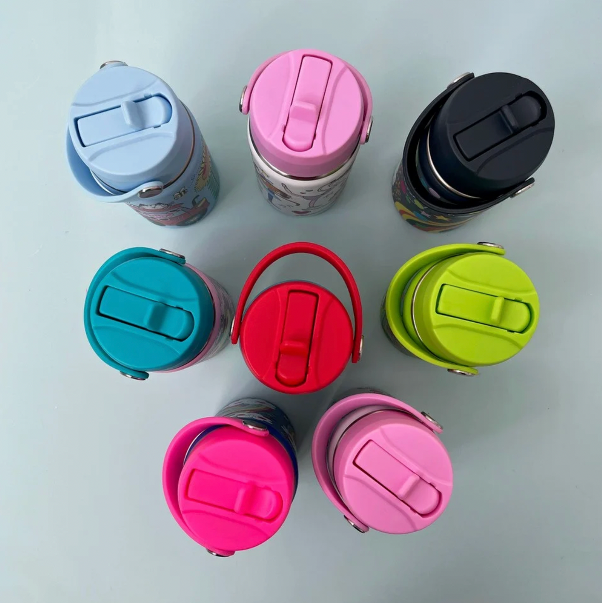 Eight Rachel Ellen bottle lids seen from above with straws folded closed: pale blue, pink and navy in top row, turquoise, red and lime-green in middle, fuchsia and pale pink below; carry handles attached with silver pivots.