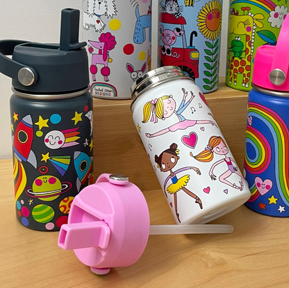 Open Rachel Ellen Ballet white bottle leaning on a wooden display, illustrated with dancers and pink hearts; detached pink straw lid and clear tube in foreground, navy space bottle at left, blue rainbow bottle at right and dog, farm and animal bottles behind.⠋