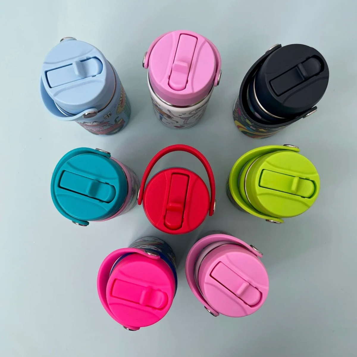 Eight Rachel Ellen water bottles viewed from above with closed straw lids: pale blue, pink and navy at top, turquoise, red and lime-green in middle, fuchsia and pale pink below; curved carry handles and silver attachment pivots visible.