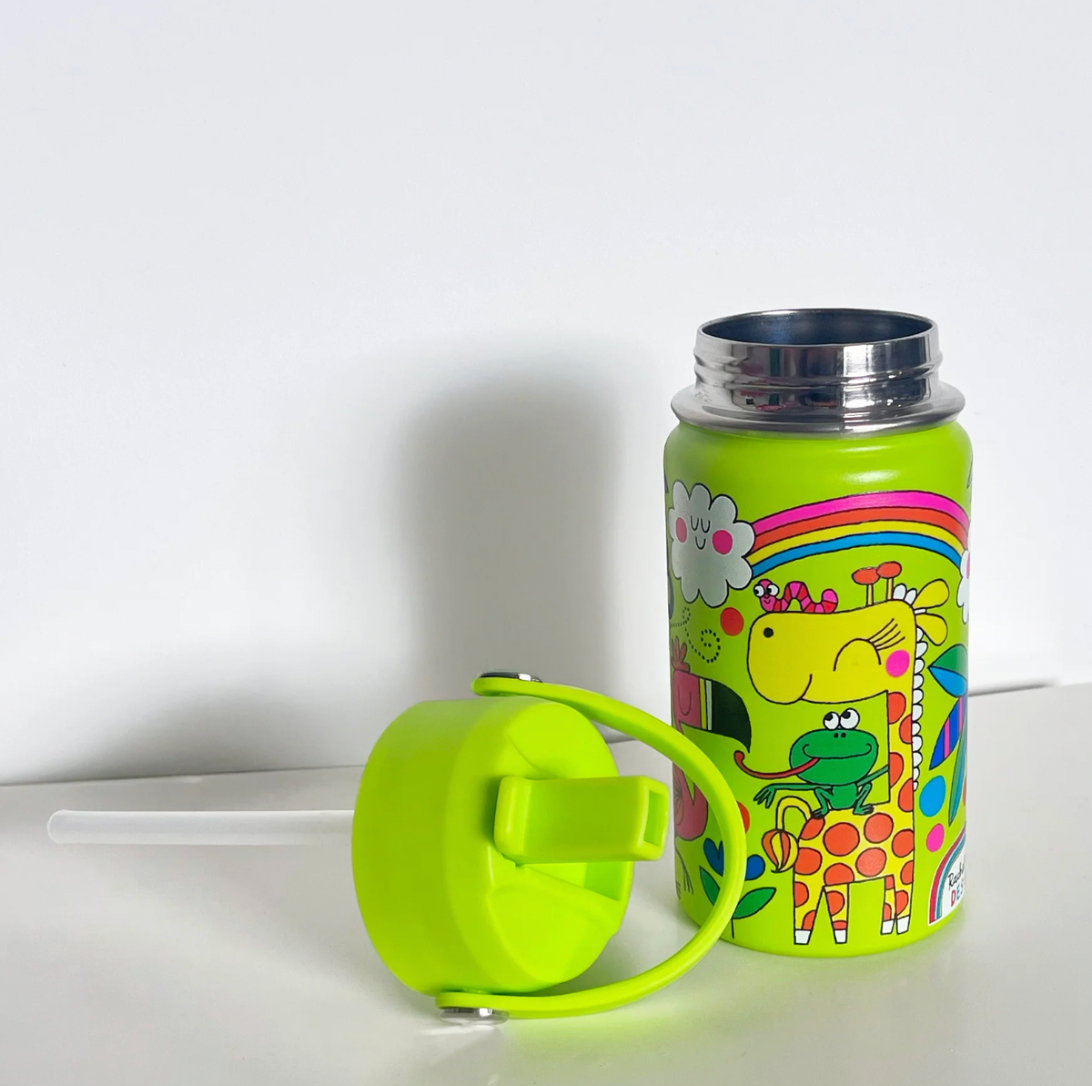 Open Rachel Ellen Jungle lime-green bottle on a white shelf, showing polished stainless steel screw threads above giraffe and frog print; detached green lid with curved handle rests in front and long clear straw extends to the left.