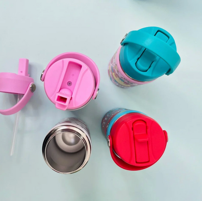 Overhead Rachel Ellen bottle detail on pale blue surface: open stainless steel bottle at lower left, detached pink lid with clear internal straw at far left, raised pink drinking spout above, turquoise closed lid at upper right and red Dinosaur closed lid at lower right.