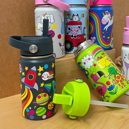 Rachel Ellen Space bottle at front left of wooden display, showing red rocket, smiling planets and dark raised straw; open lime-green Jungle bottle leans right beside detached green lid and clear straw, with Dogs, Farm and Unicorn bottles standing behind.