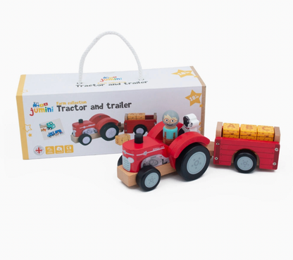 Jumini red wooden tractor and trailer in front of white gift box with rope handle, multicoloured Jumini logo, Tractor and trailer title, yellow star decoration and Union Jack emblem; farmer and black-and-white dog seated aboard, three yellow hay bales lined up in trailer.