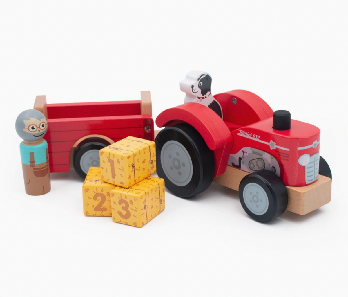 Jumini wooden farm set on white background: red tractor facing right with black exhaust, grey engine print and large black rear wheels; dog seated behind, empty red trailer at left, farmer beside it and three yellow bales stacked in front displaying numbers 1, 2 and 3.