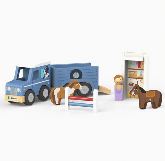 Jumini blue wooden jeep and open horse trailer on white background, with black wheels, grey hubs, printed dog in jeep window and JUMINI front plate; chestnut-and-white horse beside red-and-blue jump fence, peg person in purple dungarees, brown saddled horse and detached white roof upright as illustrated tack storage.