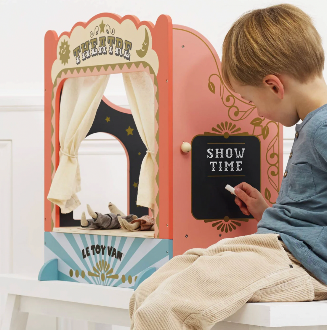 Child playing with a Le Toy Van puppet theatre set in a bright room. TABLETOP PUPPET THEATRE | LE TOY VAN