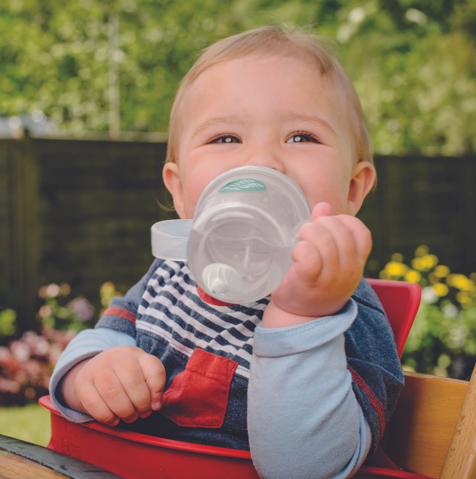 Child holding a sippy cup outdoors with greenery in the background. TIPPY CUP WITH STRAW AND FLIP TOP LEAKPROOF LID- KEV KOALA | TUM TUM