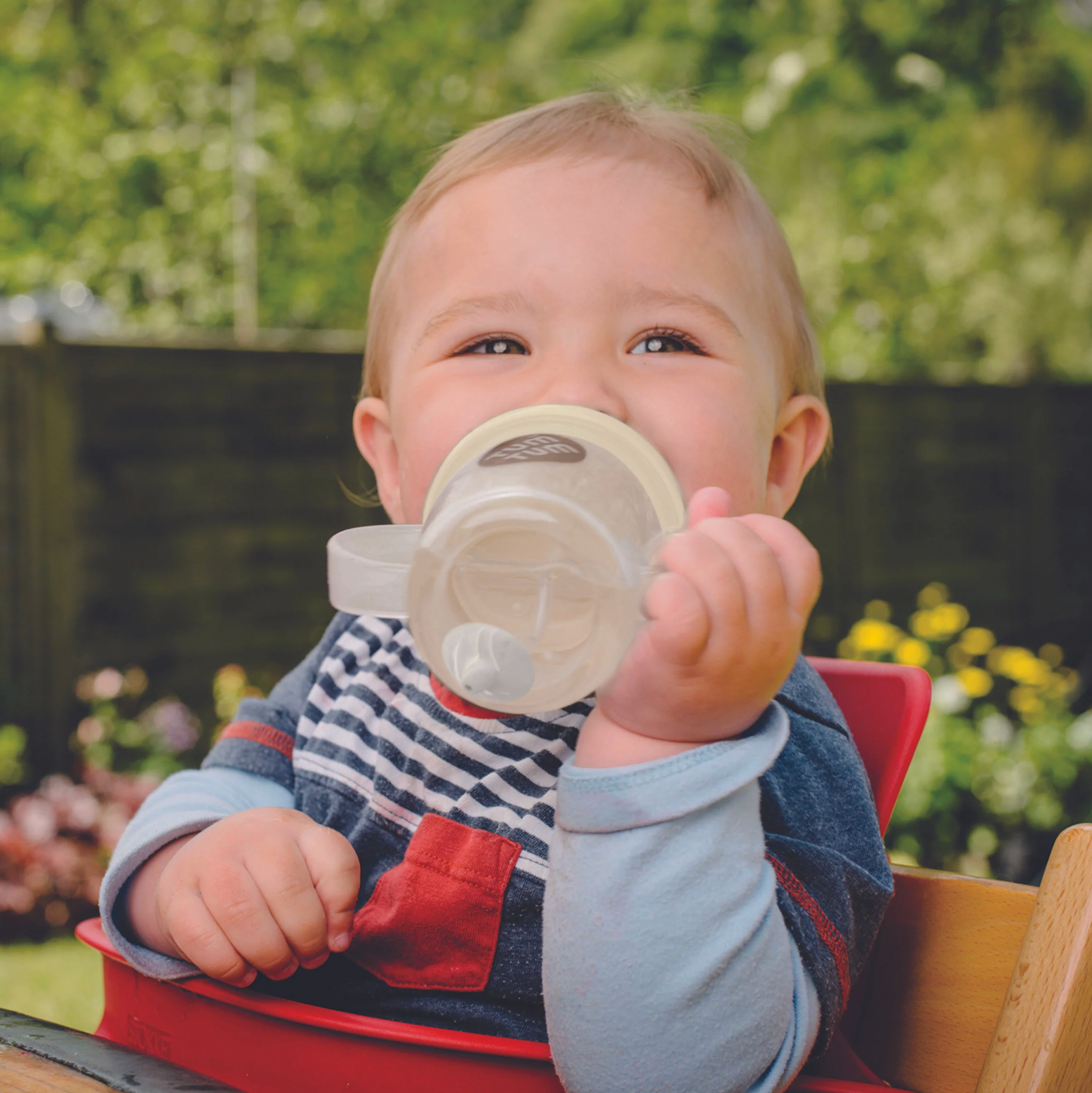 Child holding a sippy cup outdoors with greenery in the background. TIPPY CUP WITH STRAW AND FLIP TOP LEAKPROOF LID - PETE POLAR BEAR (GLOW IN THE DARK)  | TUM TUM