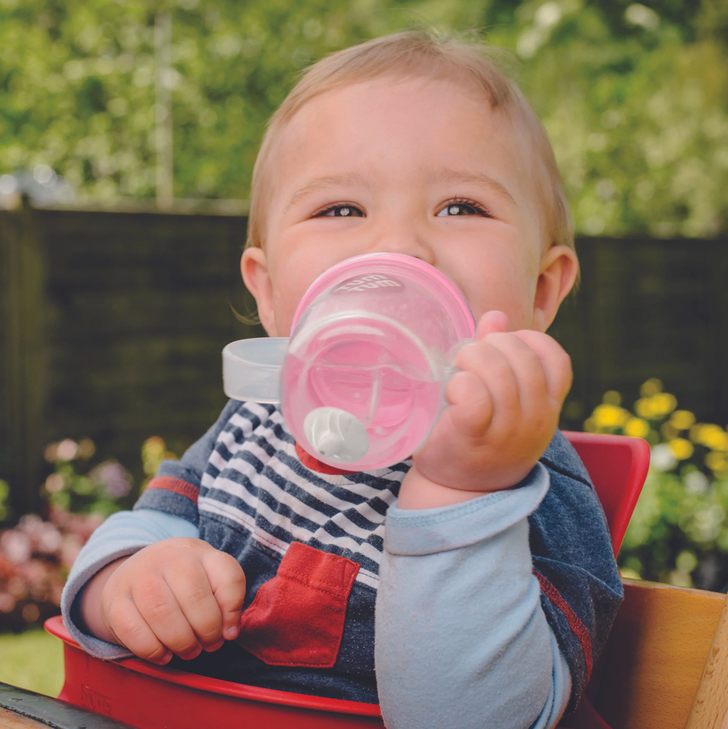 Child holding a pink sippy cup outdoors with greenery in the background. TIPPY CUP WITH STRAW AND FLIP TOP LEAKPROOF LID - PINK BETSY BEAR | TUM TUM