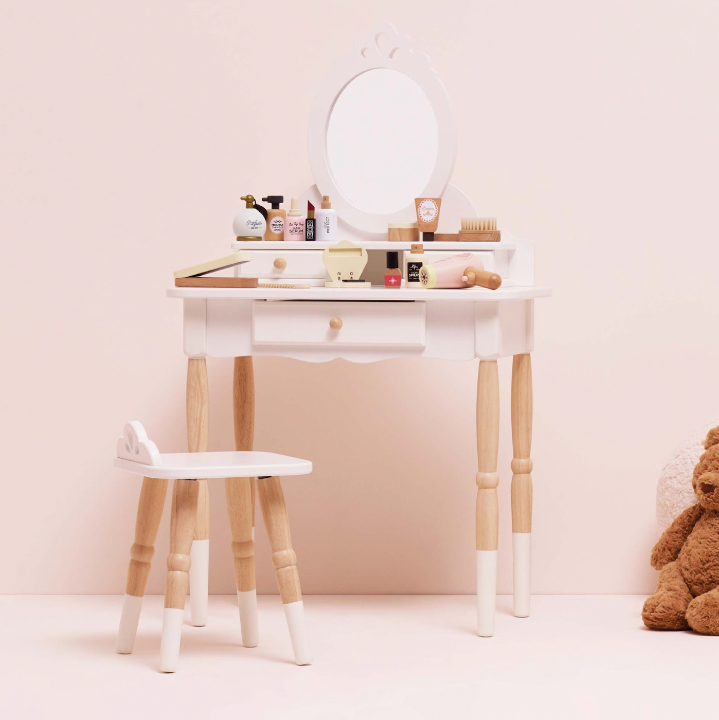 Small vanity table with mirror and stool against a light pink wall, teddy bear on the side. VANITY STAR BEAUTY KIT & WOODEN ACCESSORIES | LE TOY VAN