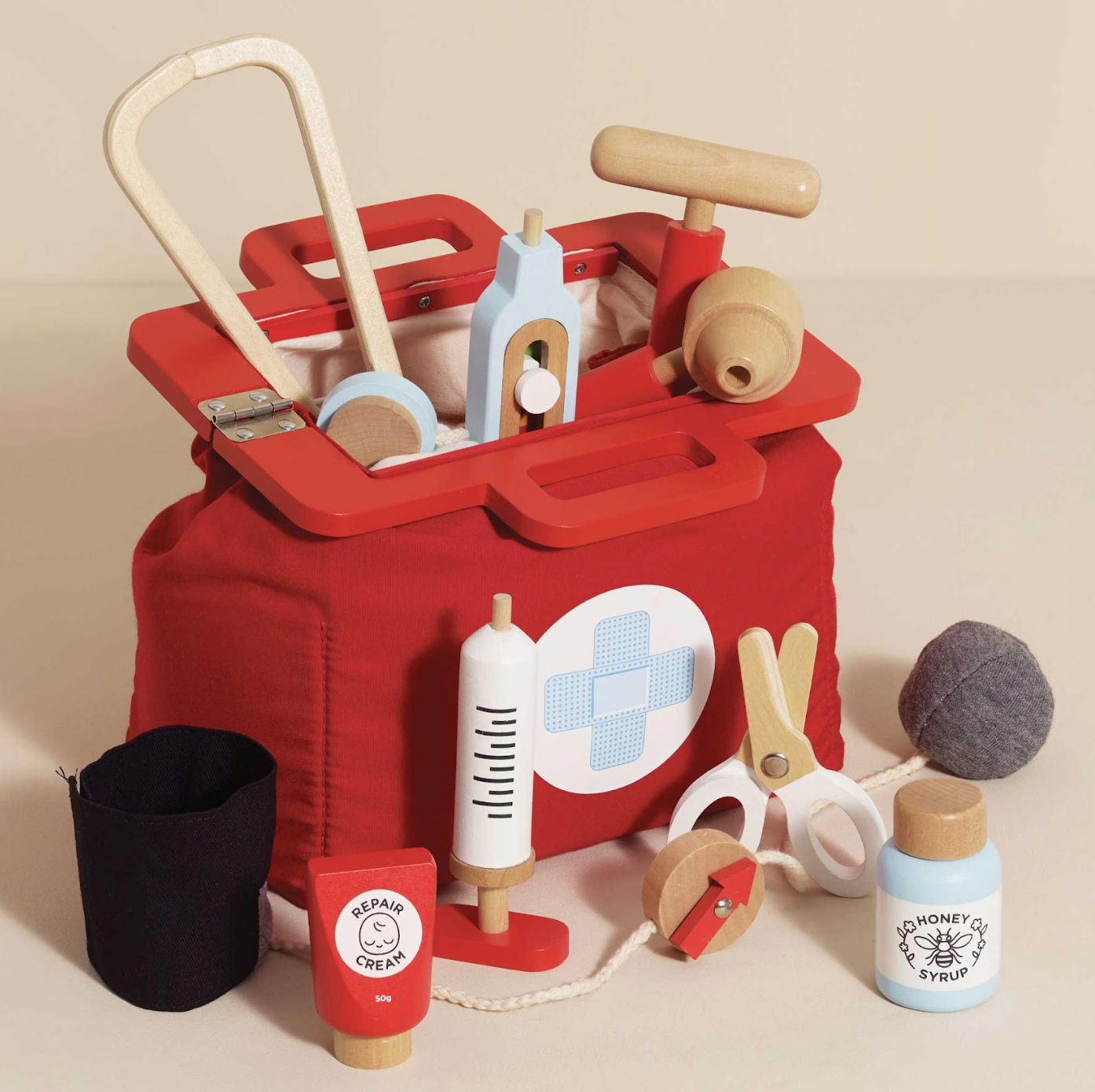 Red toy first aid kit with various wooden items on a beige background. VINTAGE DOCTOR ROLEPLAY KIT | LE TOY VAN