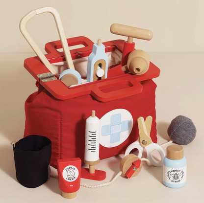 Red toy first aid kit with various wooden items on a beige background. VINTAGE DOCTOR ROLEPLAY KIT | LE TOY VAN