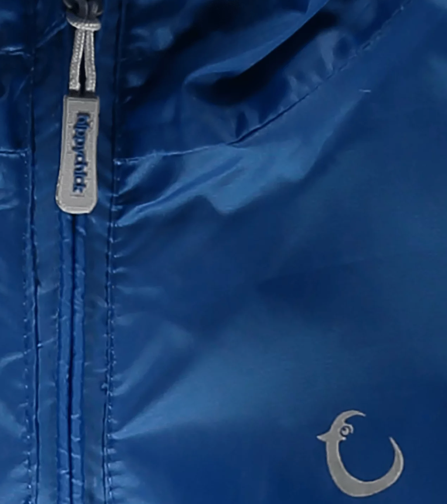Close-up of a blue jacket with a brand logo on a dark background. WATERPROOF TODDLER ALL-IN-ONE PACKASUITS - BLUE | HIPPYCHICK 