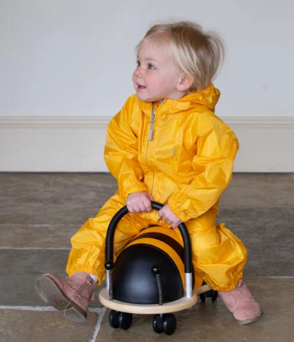 Hippychick Yellow kids rain suit with hood and a matching pouch - child playing with a ride on toy. WATERPROOF TODDLER ALL-IN-ONE PACKASUITS - YELLOW | HIPPYCHICK 