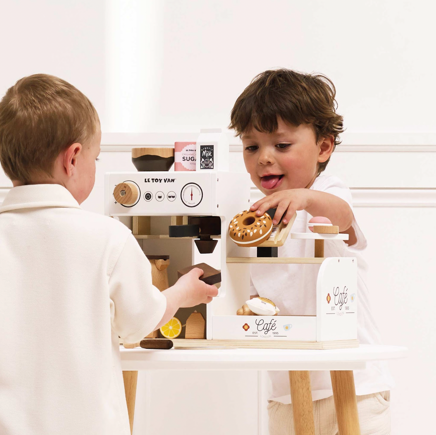 Two children playing with a toy kitchen set on a white background. WOODEN BARISTA CAFE SHOP | LE TOY VAN