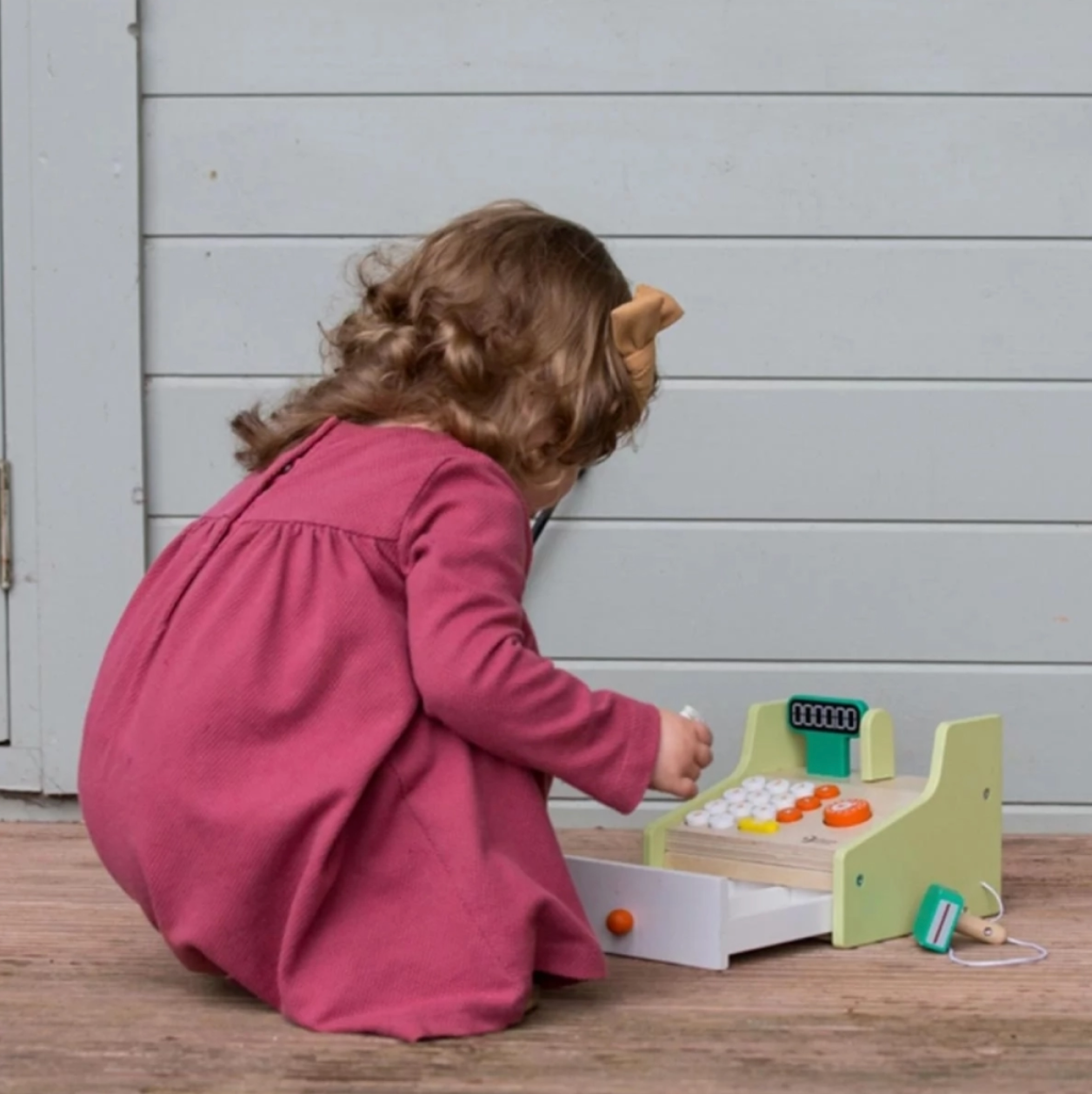 Child playing with a wooden toy on a wooden floor. WOODEN CASH REGISTER TOY | CLASSIC WORLD 