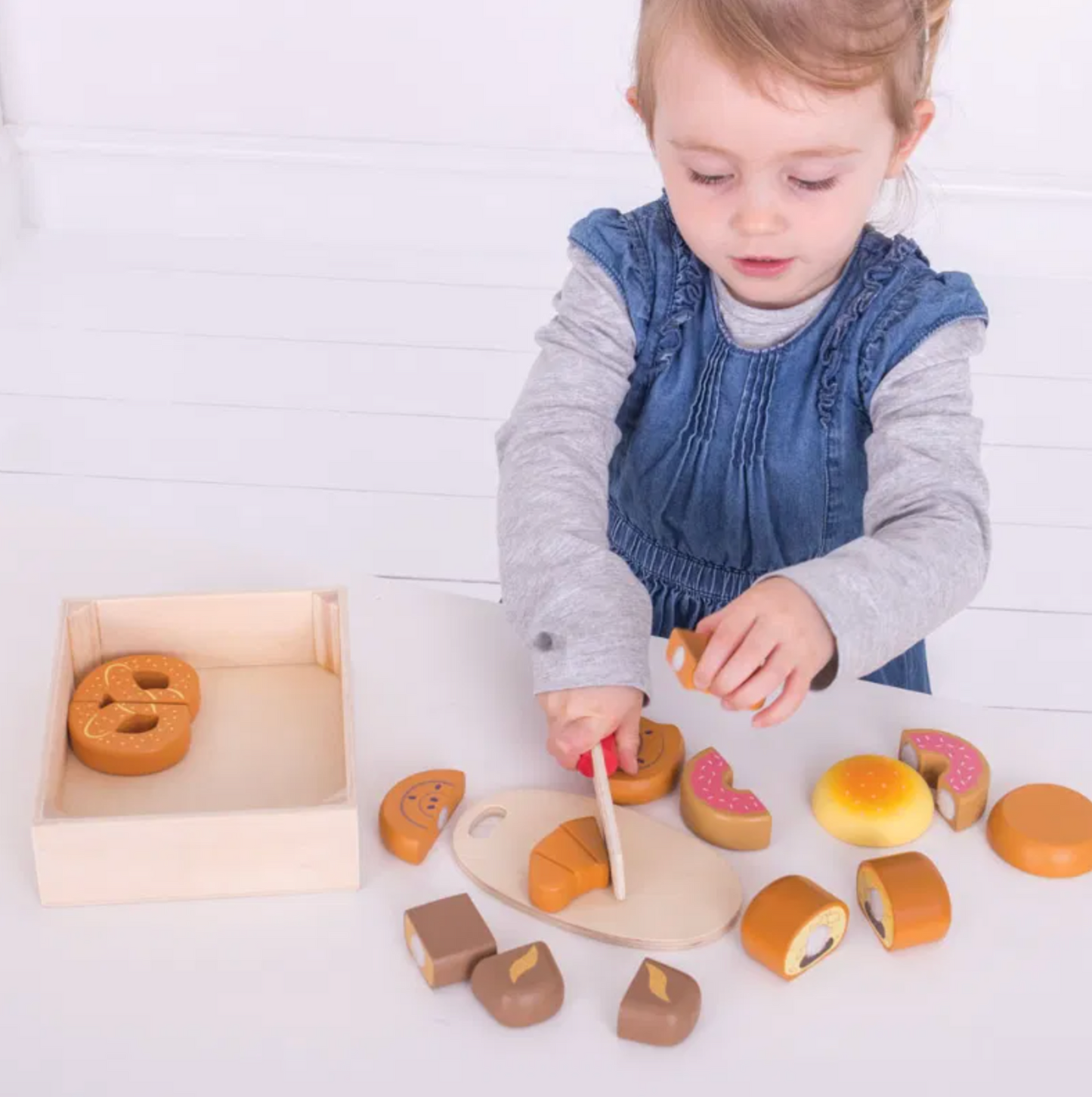 Child playing with wooden toy food items. WOODEN CUTTING BREAD AND PASTRIES CRATE PLAY FOOD  | BIGJIGS