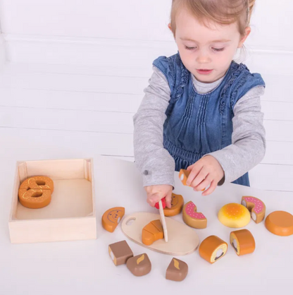 Child playing with wooden toy food items. WOODEN CUTTING BREAD AND PASTRIES CRATE PLAY FOOD  | BIGJIGS
