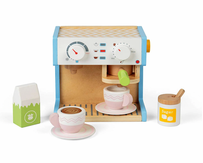 Bigjigs wooden espresso coffee maker play set — three-quarter view on white background showing the natural birch wood machine body with pale blue side panels, white front panel printed with temperature gauge dial, Min/Max dial, indicator lights and coffee cup icons, natural wood slatted drip tray, and green portafilter handle in the group head slot with yellow toggle switch on the right side; accessories displayed around the machine: two blush pink chevron-pattern cups with latte art swirl inside on matchin