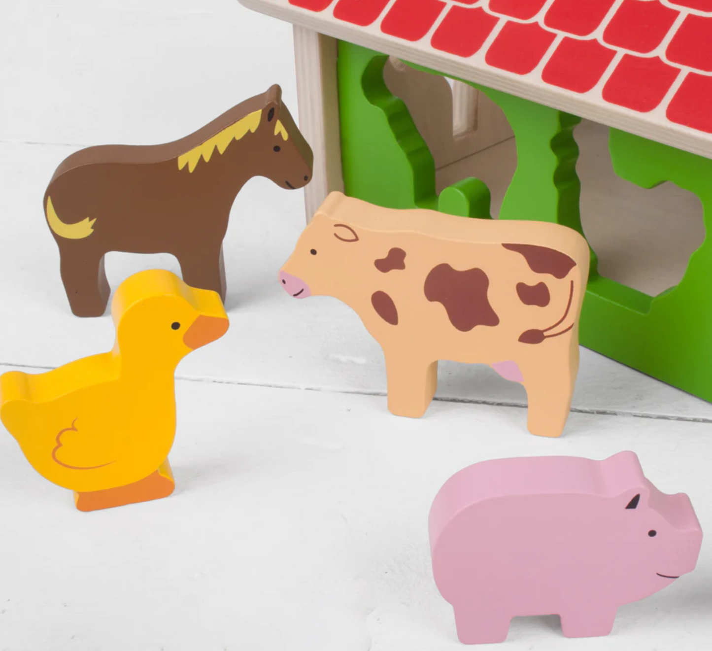 Wooden farm animal toys including a horse, cow, duck, and pig in front of a green barn. WOODEN FARMHOUSE SORTER | BIGJIGS