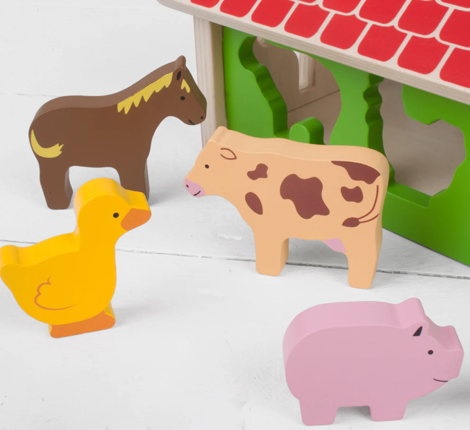 Wooden farm animal toys including a horse, cow, duck, and pig in front of a green barn. WOODEN FARMHOUSE SORTER | BIGJIGS
